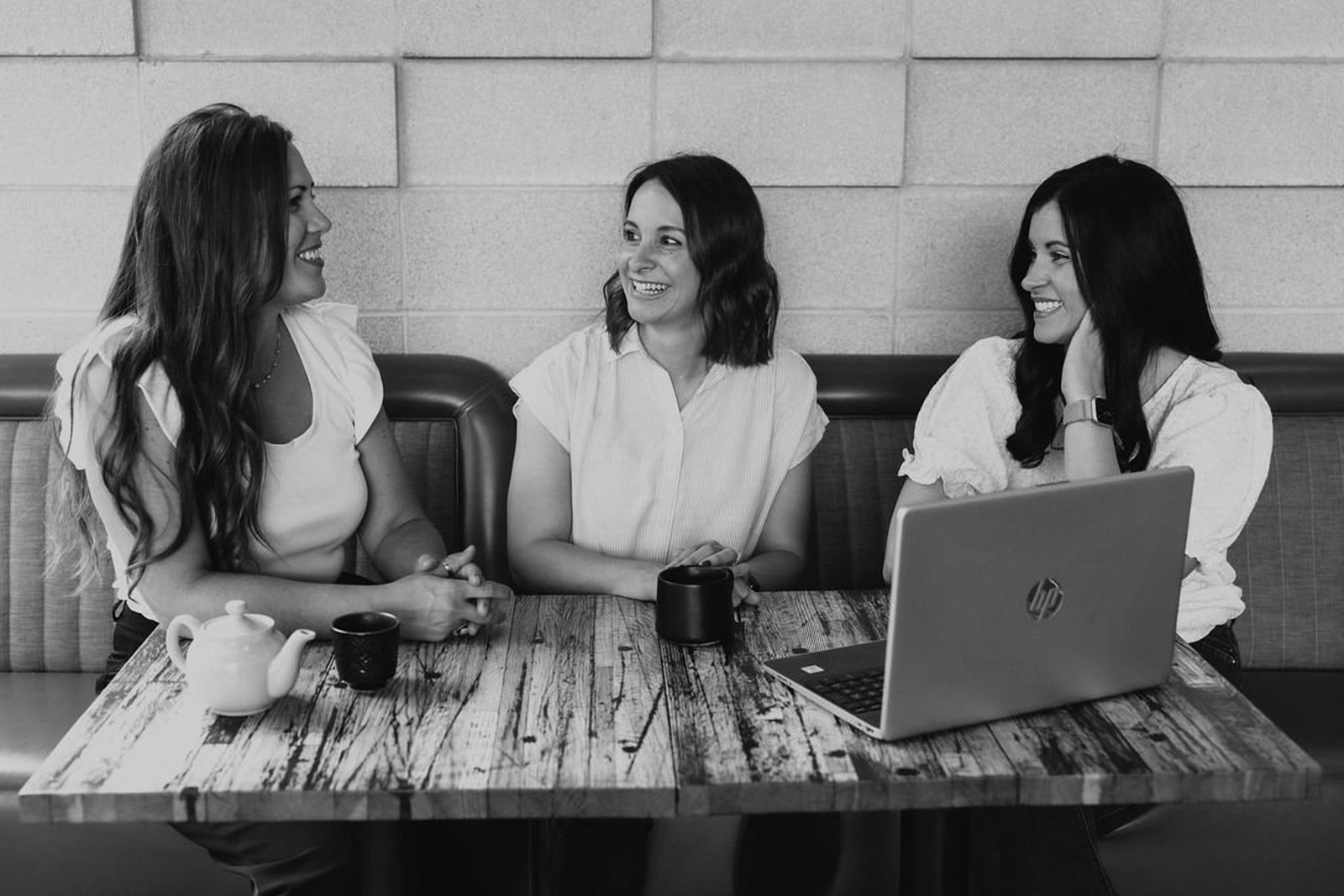 Black and white photograph of Erin, Keri and a designer talking together over a laptop at a restaurant table